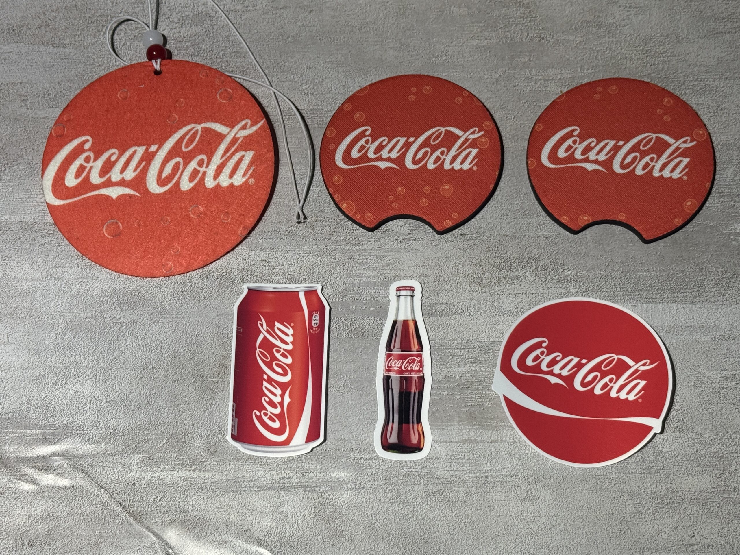 A set of matching car accessories and stickers, featuring a pink graphic design. The set includes one hanging car air freshener, two round cup holder coasters, and three vinyl stickers.